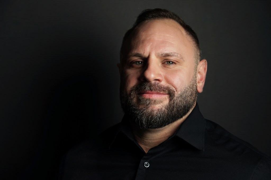Professional headshot of a bearded man wearing a black shirt with a black background in Phoenix Arizona