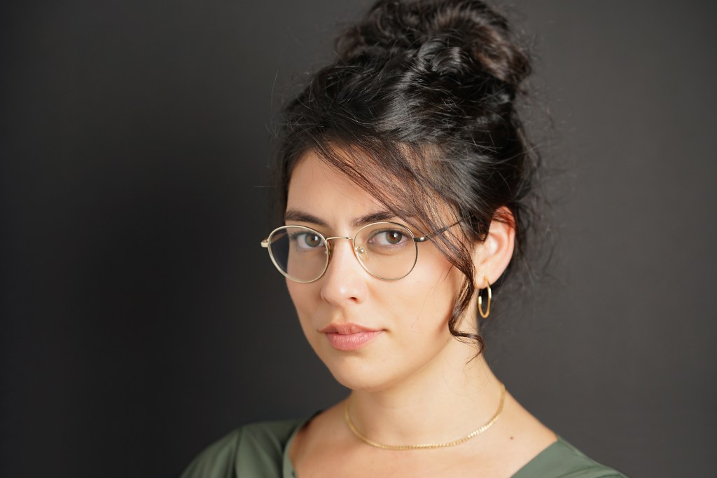 Headshot Portrait of a mixed race Arab woman with curly hair and glasses with black background in Phoenix Arizona