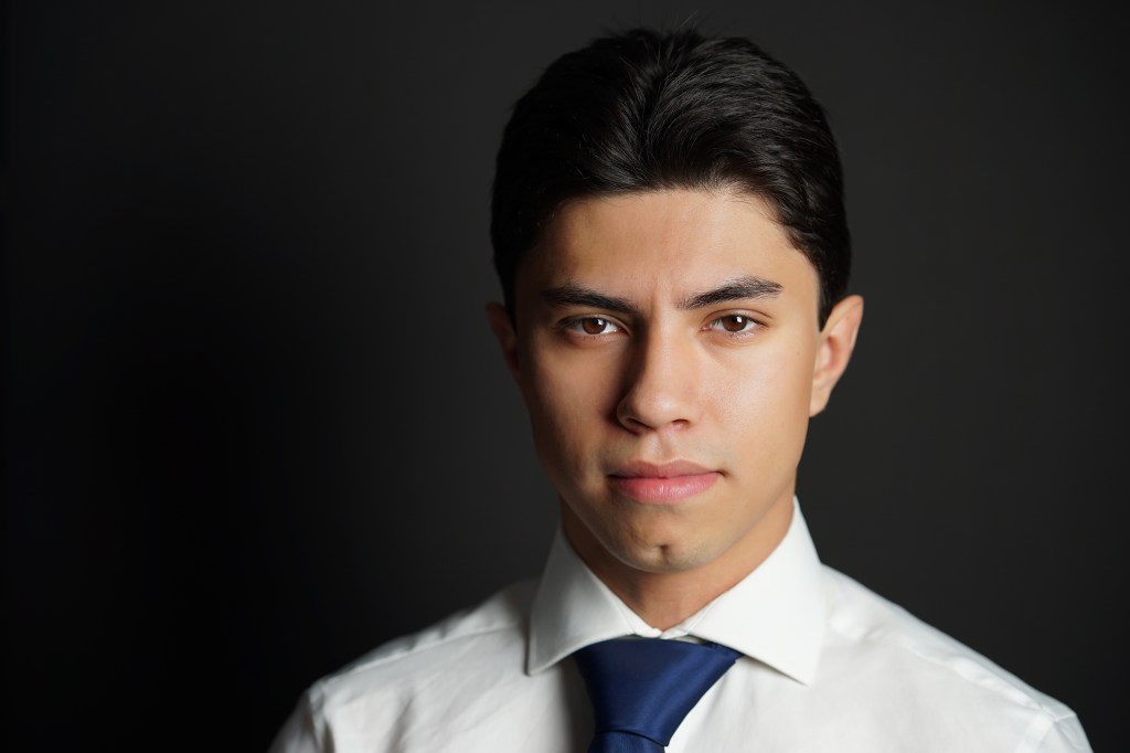 Professional headshot of a handsome young Mexican man wearing a white shirt and blue tie with black background in Phoenix Arizona
