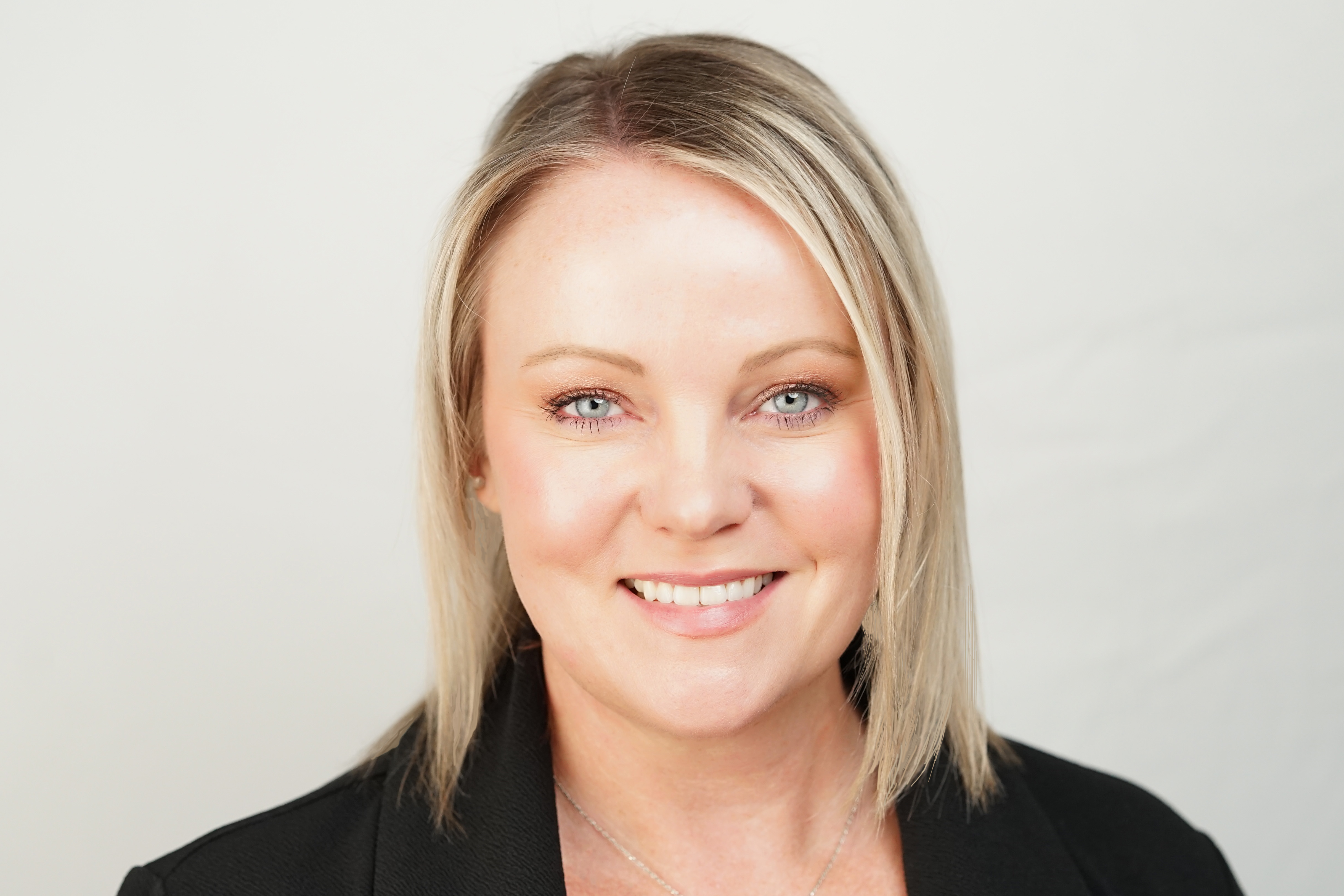 Professional headshot of blond woman with blue eyes smiling wearing a black blazer who is an executive in Phoenix Arizona